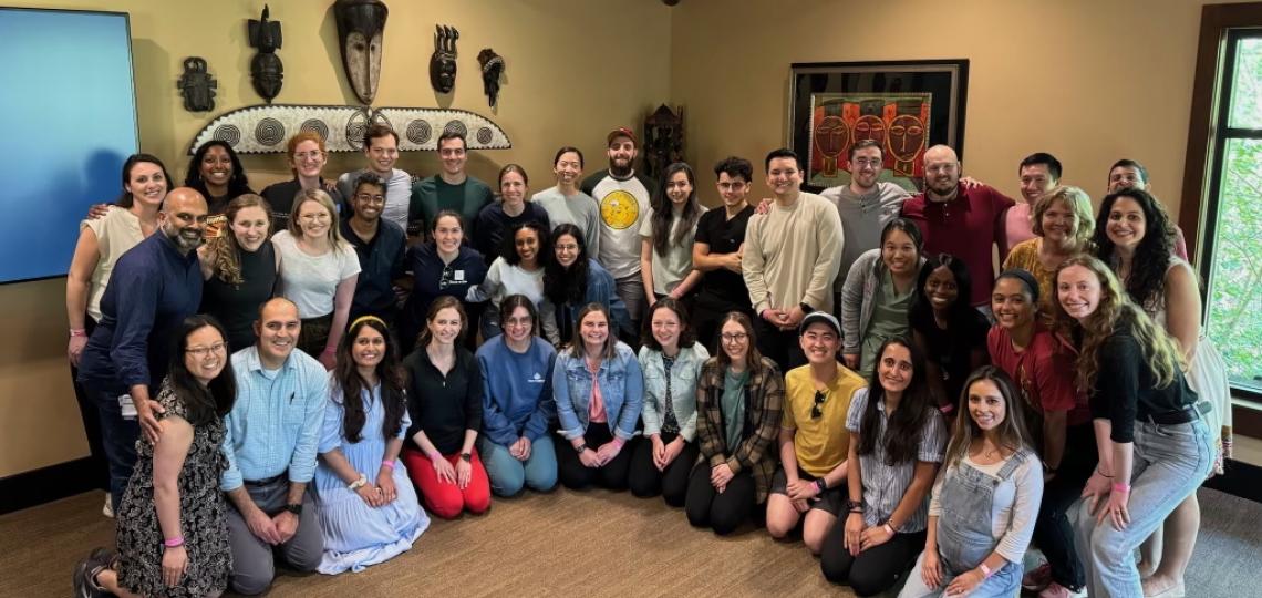 A large group of smiling students in casual clothes seated in a room filled with artwork