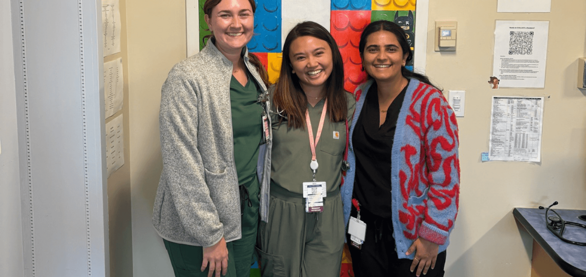 Three smiling residents standing in front of a door decorated with a poster of LEGO blocks
