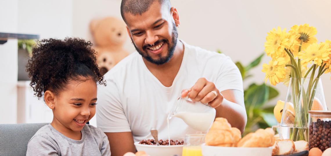 Father helping daughter make cereal