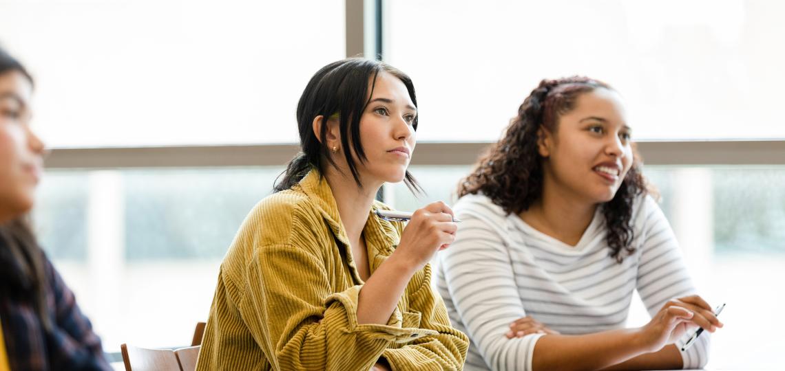 Students in a brightly-lit room listening to a lecture while taking notes.
