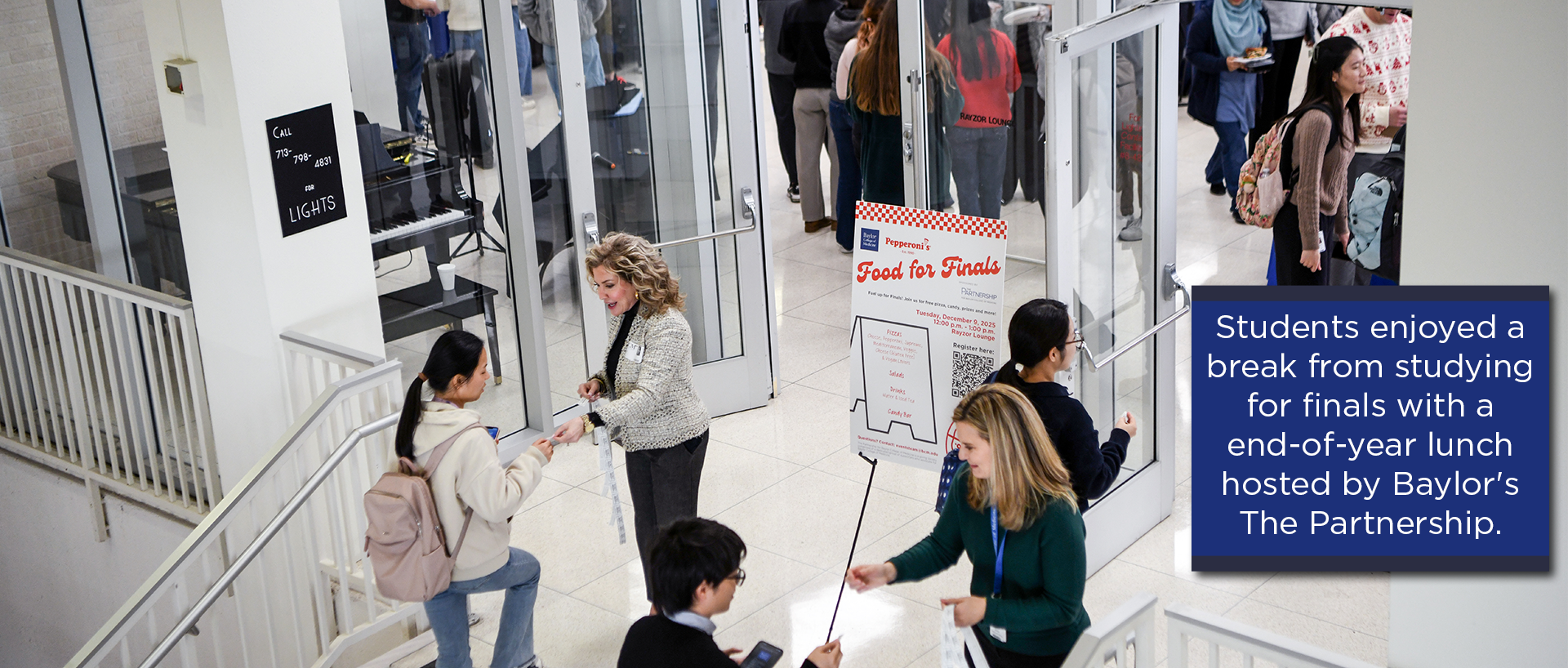 Students gather in a bright indoor space near glass doors for an event. A sign reading “Food for Finals” is displayed on an easel, indicating an end-of-year lunch hosted by Baylor’s The Partnership. Several students are seen holding plates and utensils, while others are entering or exiting the area