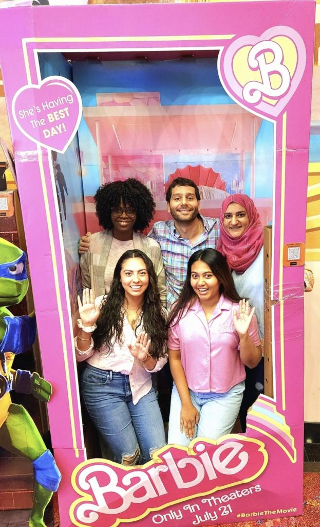 small group of people smiling in a large Barbie box