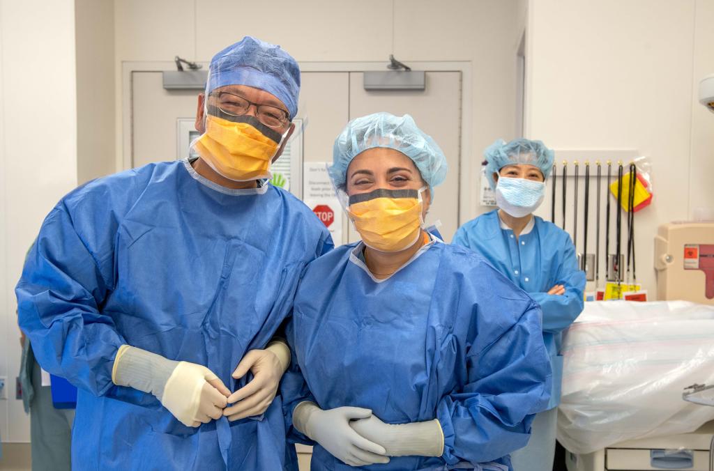 Three people wearing scrubs posing in a medical room.