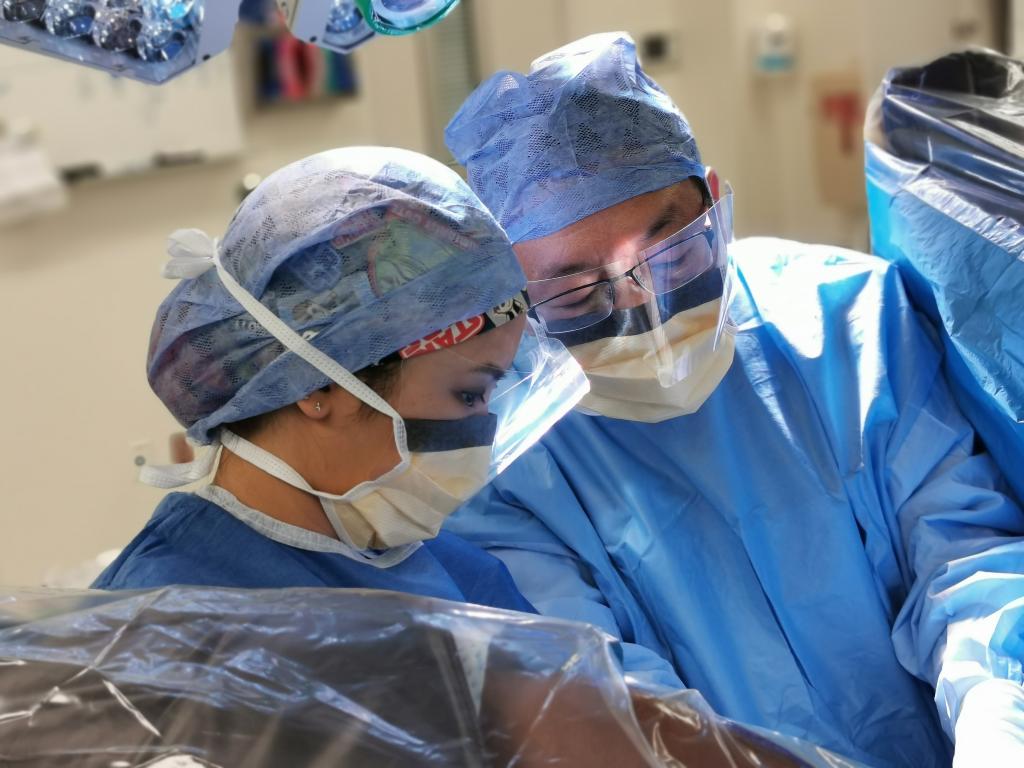 Two people wearing blue surgical scrubs looking over an exam table.