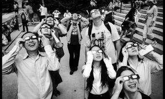 Photo of a group of people wearing solar eclipse glasses looking up at the sky.