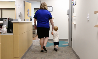 A doctor leads a child into an office to be screened with a Modified Checklist for Autism in Toddler, or M-CHAT.