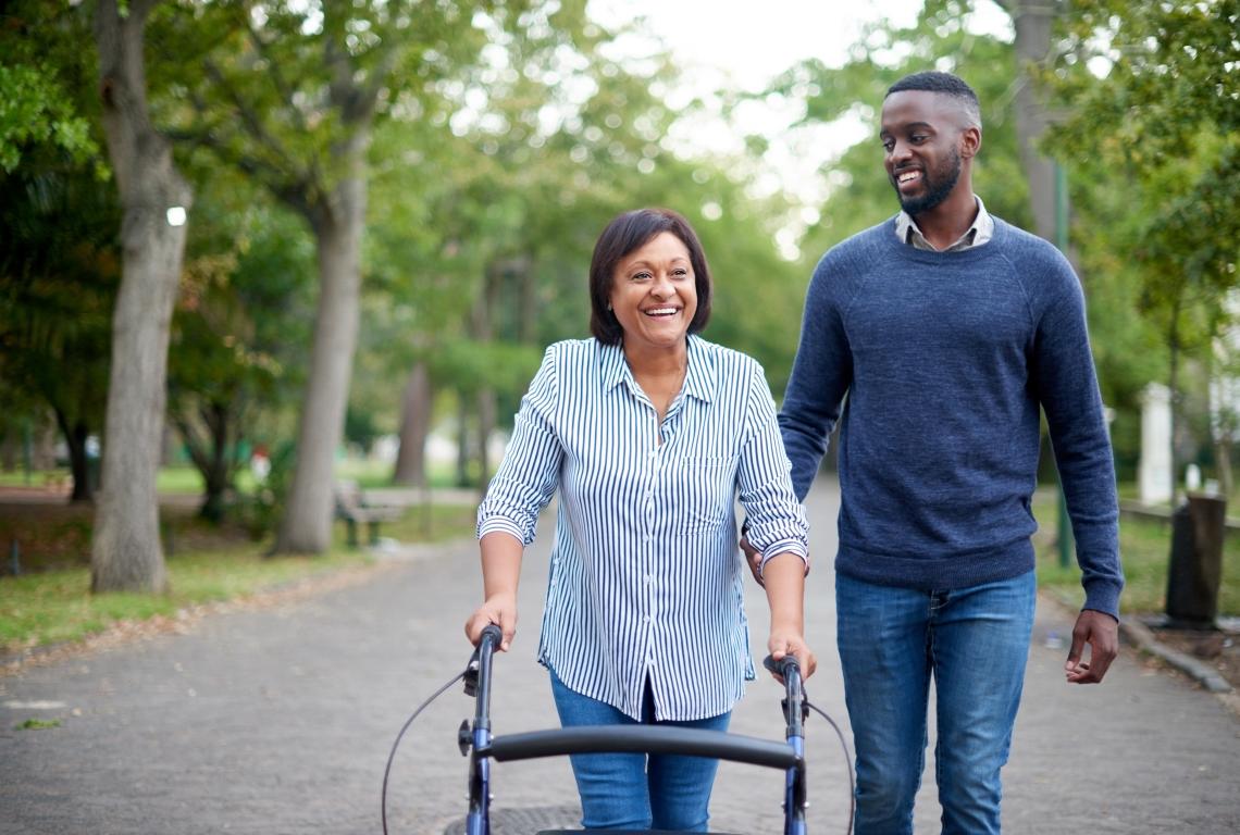 A woman walking with a walker assisted by a loved one. 