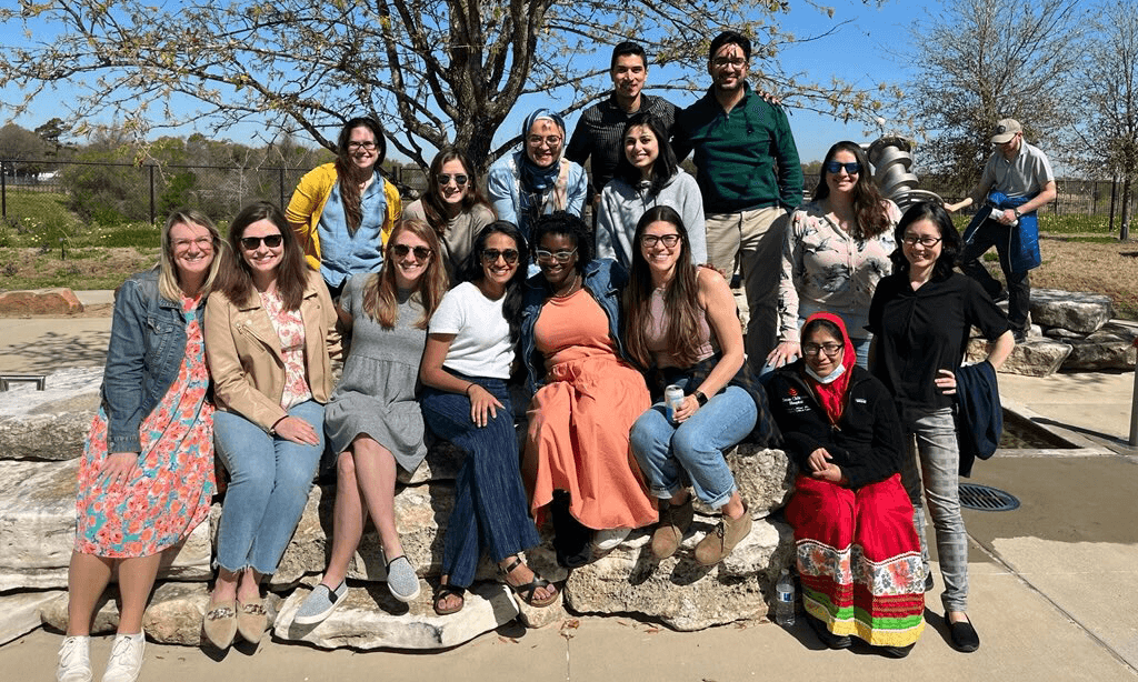 A group of Pediatric Critical Care Fellows pose in a line outside on a pile of rocks.