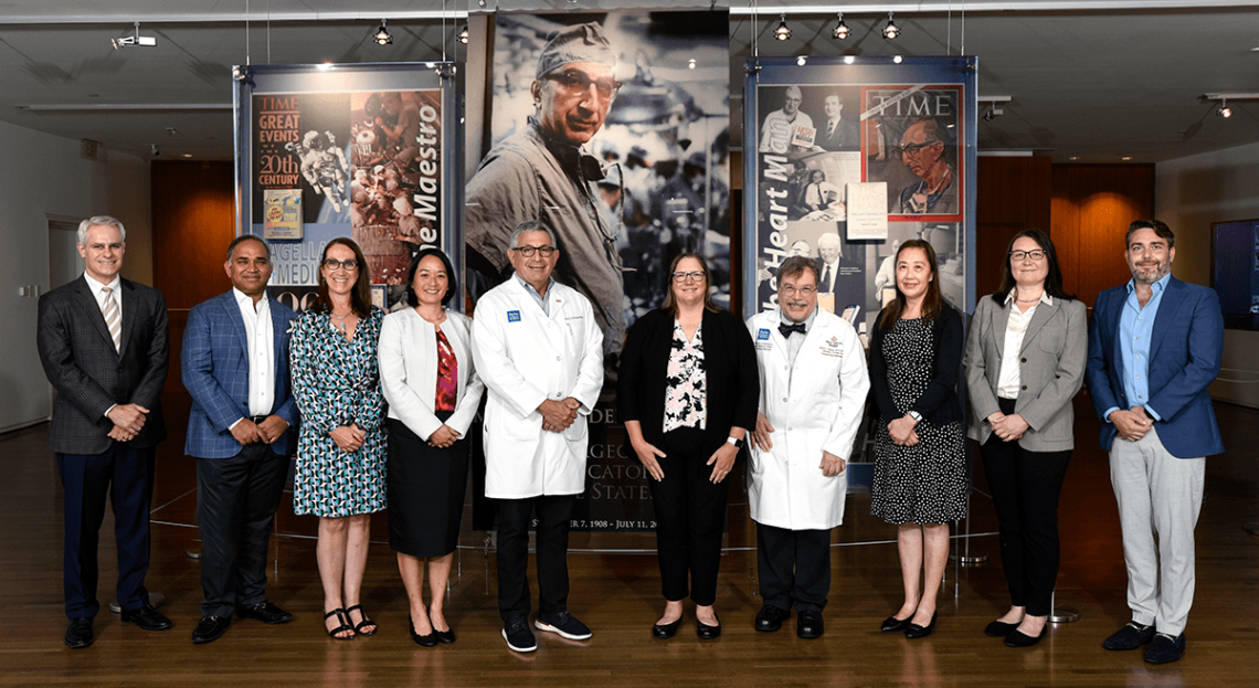 The Michael E. DeBakey Excellence in Research Award winners pose in a line in front of a large picture of Dr. DeBakey.