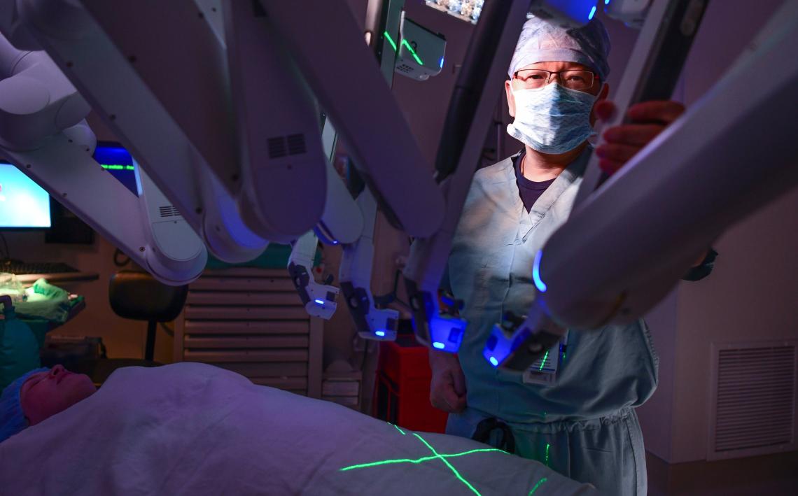 Dr. Xiaoming Guan, an expert in robotic surgery for treating endometriosis stands behind a surgical robotic mechanism.