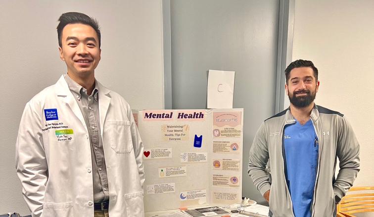 Two volunteers from psychiatry stand in front of an information booth about mental health