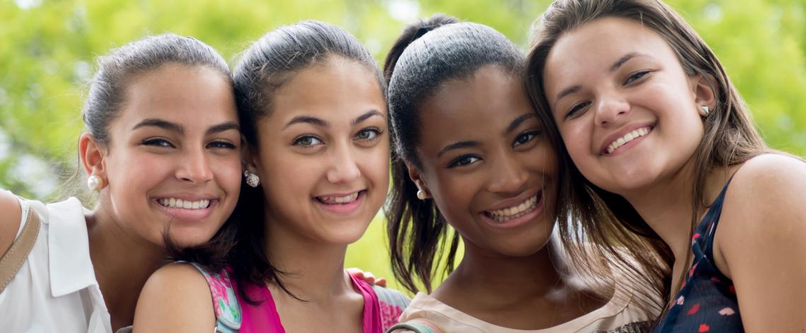 Four teen girls of diverse ethnicity standing close together.