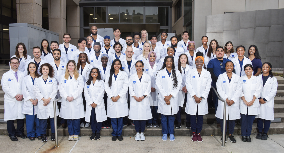The 2023 Emergency Medicine Residents stand together on steps while wearing white coats.