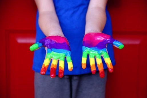 This image shows a child's hands painted with the colors of the rainbow.