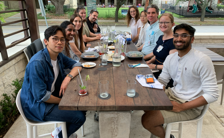 Ten members of the Bijanki Lab seated at a long table outdoors, eating lunch together.