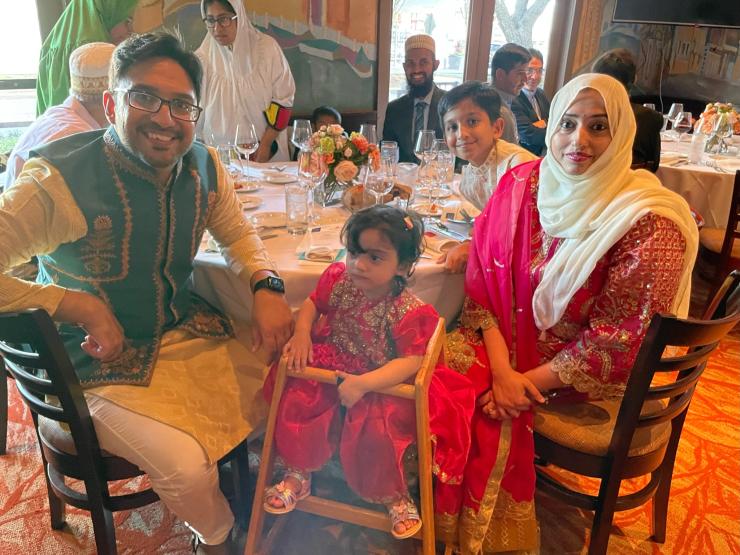 A member of the Pediatric Critical Care Fellowship poses with their family, including a child in a high chair, during an event at a restaurant