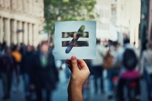 A hand holding up a piece of paper with an inequality sign in front of a crowd of people.