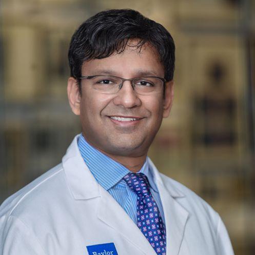 man wearing a white coat smiling in front of brown background