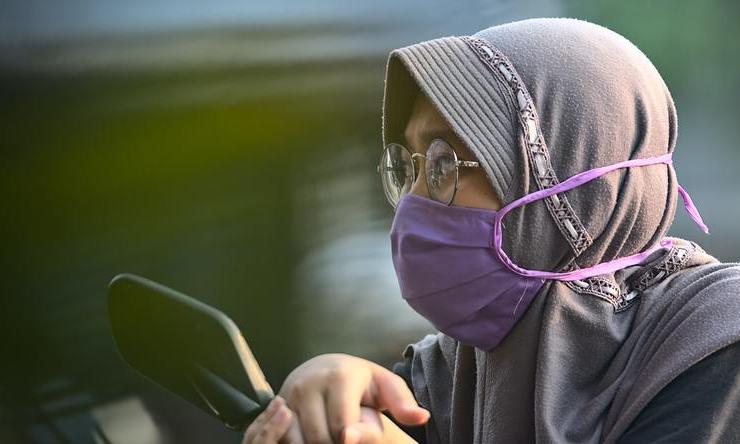 A person wearing a purple protective face mask while sitting on a motorcycle.