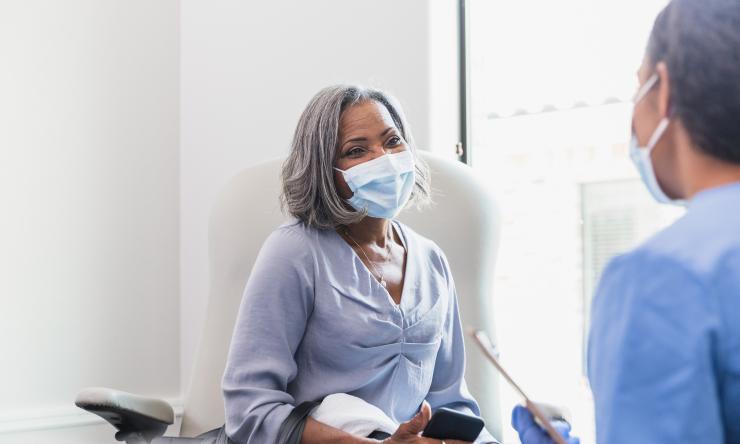 Older female patient wearing a mask over her face and phone in her hand speaking with healthcare professional