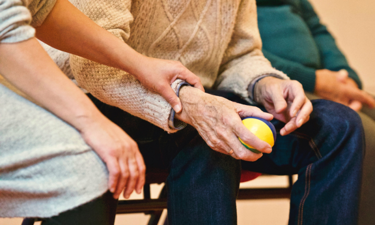 An older person holding a ball while being assisted by a caregiver