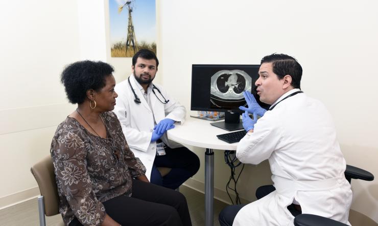 Two male doctors discussing a medical image of the inside of the body with a female patient