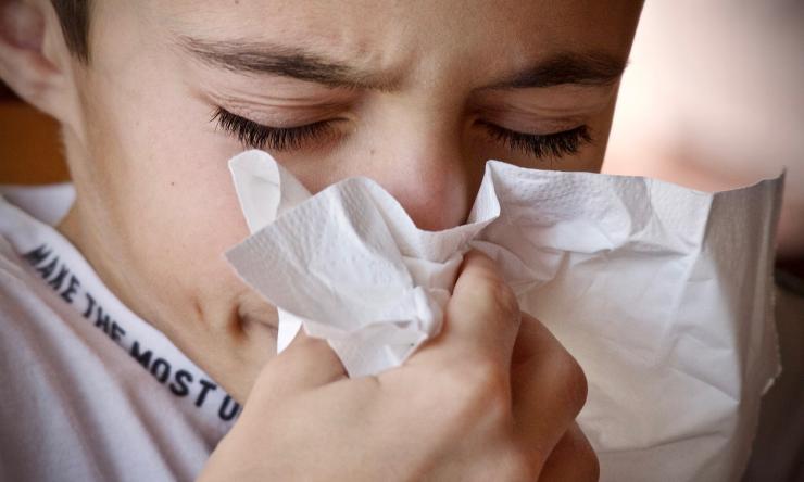 Image of a young boy sneezing into a tissue.