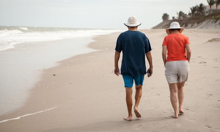 Two elderly people walking on a beach.