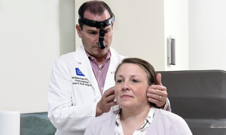 A doctor standing behind a patient while feeling the edges of their face.