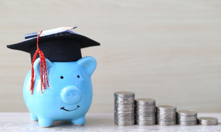 Piggy bank with a graduation cap next to stack of coins