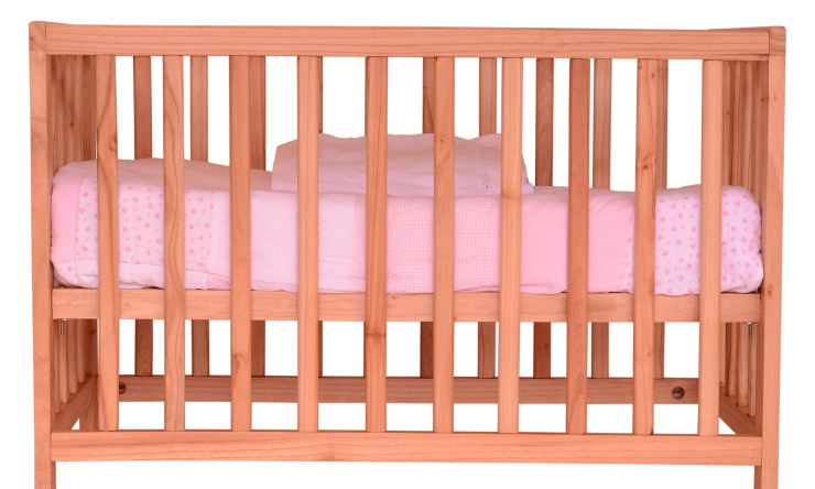 Photo of a crib, light wood with pink bedding. 
