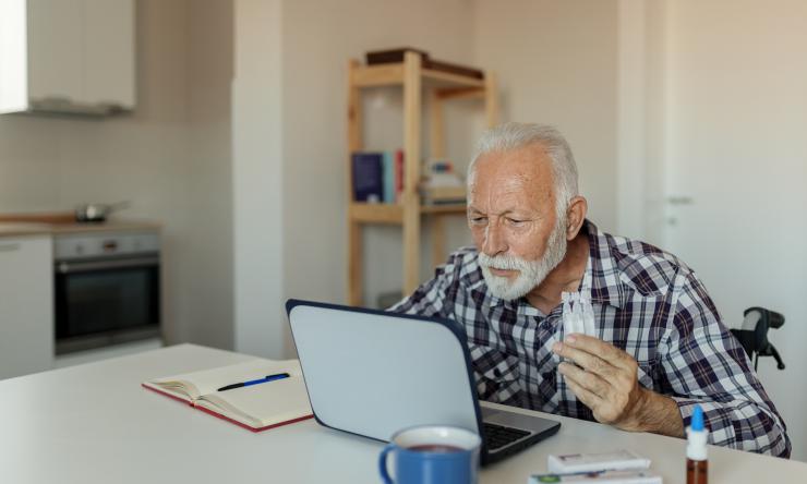 An older adult reading a laptop and taking notes on paper