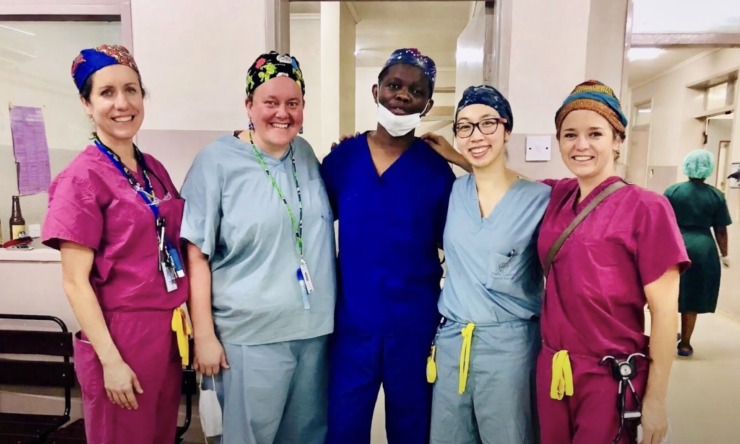 Five medical professionals in colorful scrubs smiling shoulder-to-shoulder