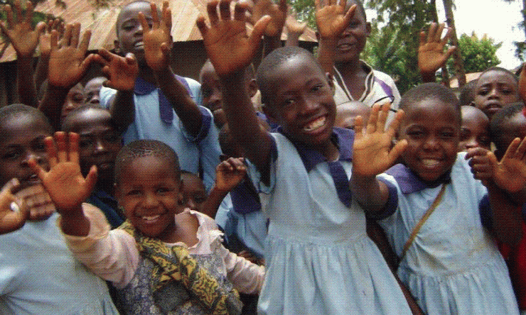 A group of Kenyan children smiling and waving at the camera