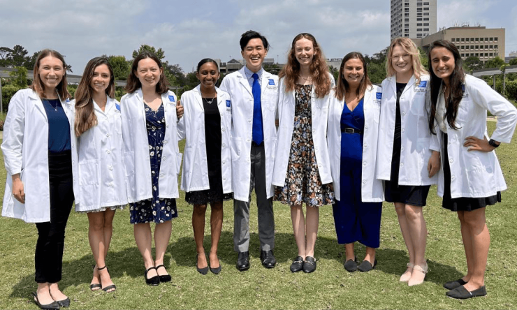Nine students in white coats posing in a grassy field 