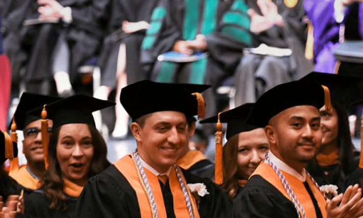 Several students wearing orange and black graduation robes