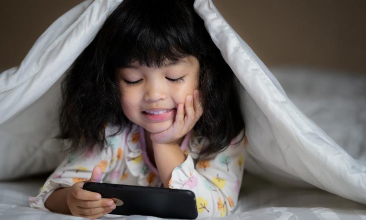 Photo of girl playing with phone under a blanket