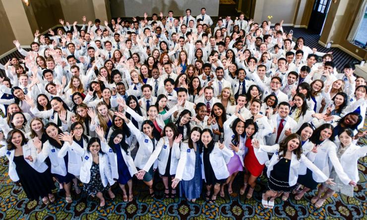 A large group of students wearing white coats gleefully posing for a photo