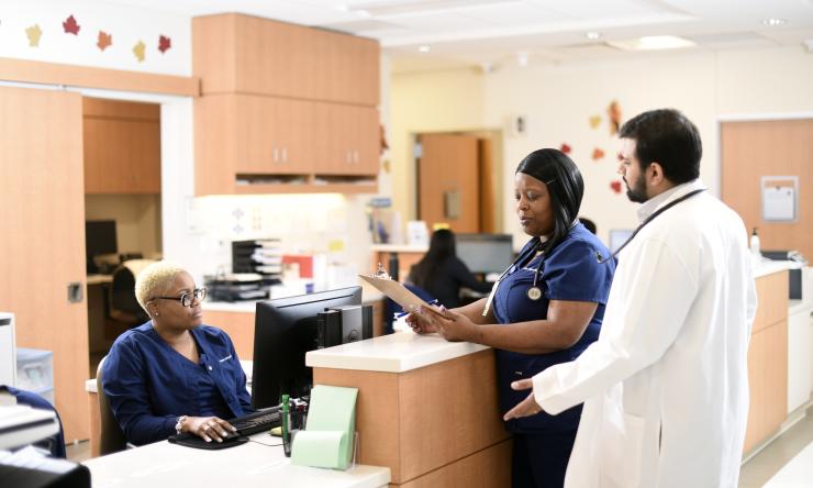 Healthcare professionals stand around a nurses station in the internal medicine clinic discussing patient care.