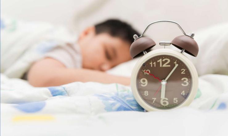 Child asleep with alarm clock in the foreground