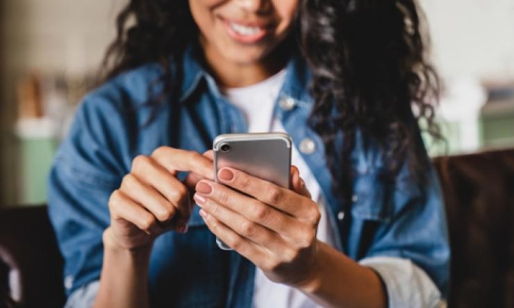 Photo of a woman holding a cell phone and smiling. 