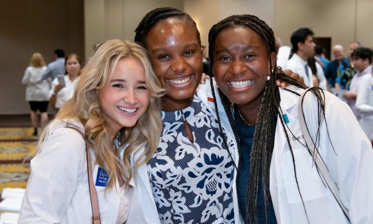 Three medical students smile and hug each other as they pose for a photo. 