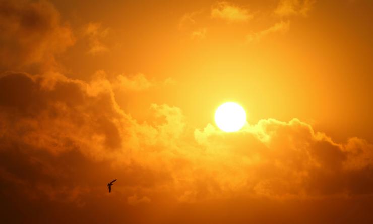 Photo of the sun with clouds in an orange haze to symbolize heat
