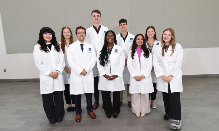 A group of smiling students wearing their white coats.