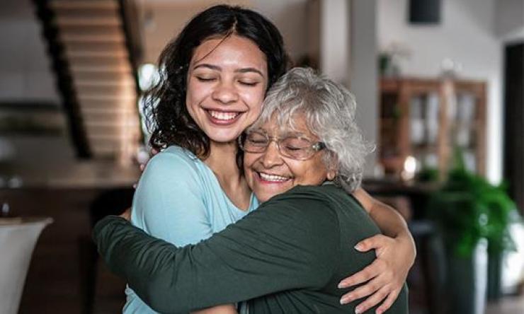 An elderly woman hugs a younger woman to represent those living with Alzheimer's disease and their family or caregivers.