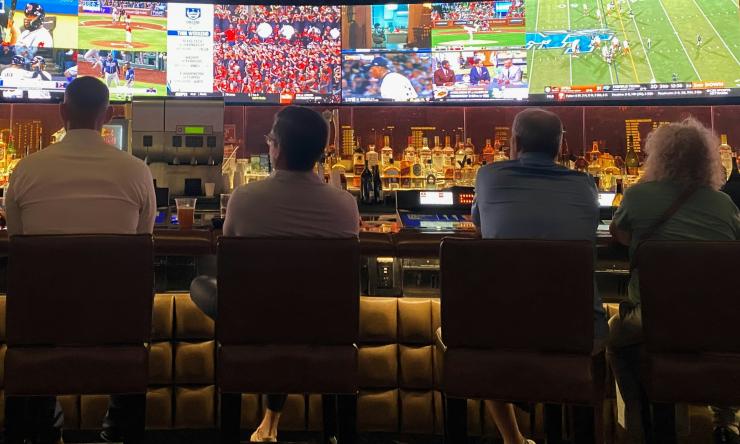 Four people sitting at bar watching sports games on TV