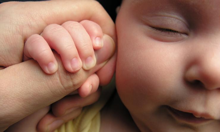 A newborn baby holds on to an adult's thumb.