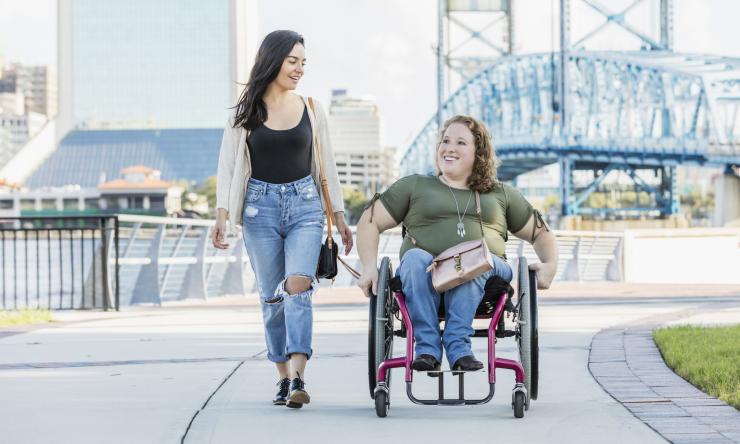 two women on a sidewalk, one in a wheelchair